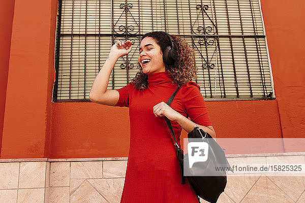 Porträt einer glücklichen Frau in rotem Kleid  die mit Kopfhörern Musik hört