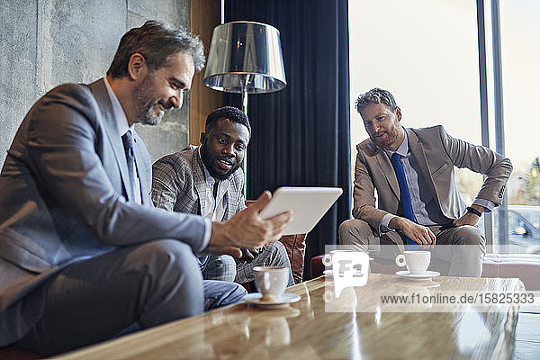 Three businessmen sitting in hotel lobby with tablet