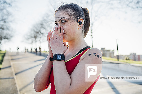 Sportliche junge Frau mit schnurlosen Kopfhörern  die sich die Nase schnäuzt