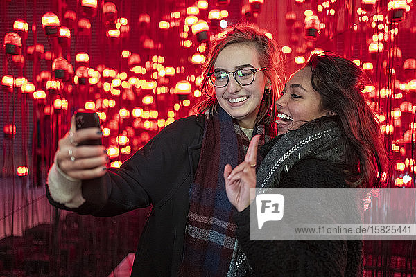 Porträt von glücklichen Freunden  die vor roten Glühbirnen ein Selfie machen