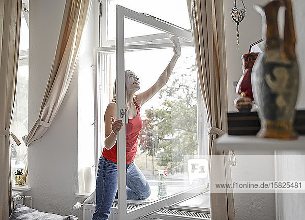 Smiling young woman cleaning window at home