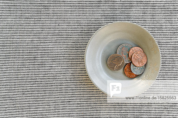 Bowl with small pile of coins on striped backgroundÂ