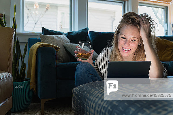 Entspannte Frau mit Wein und Blick auf ein Tablet zu Hause