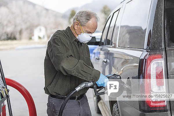 Mann mit chirurgischen Handschuhen und Maske beim Betanken eines Autos an einer Tankstelle