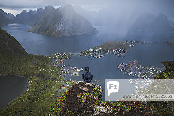 Norwegen  Lofoten  Reine  Mann blickt vom Reinebringen-Berg bei Regen auf den Fjord