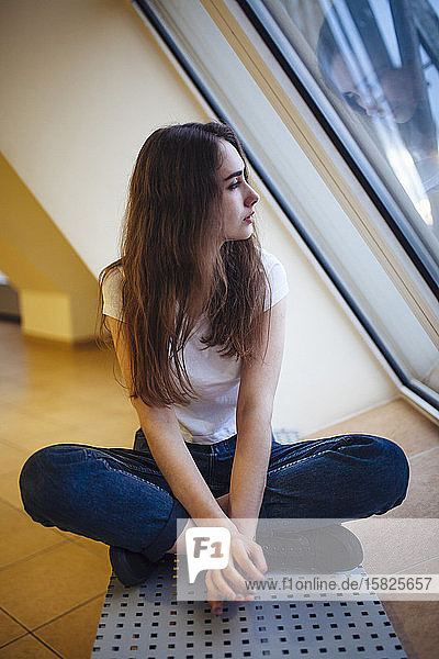 Young woman sitting on floor and looking through window