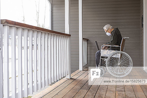 Senior man in wheelchair wearing protective mask to preventÂ coronavirusÂ transmission using laptop on porch