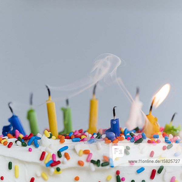 Extinguished birthday candles on cake - one still burning