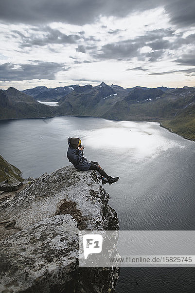 Norwegen  Senja  Mann fotografiert am Rande einer steilen Klippe auf dem Gipfel des BergesÂ Segla
