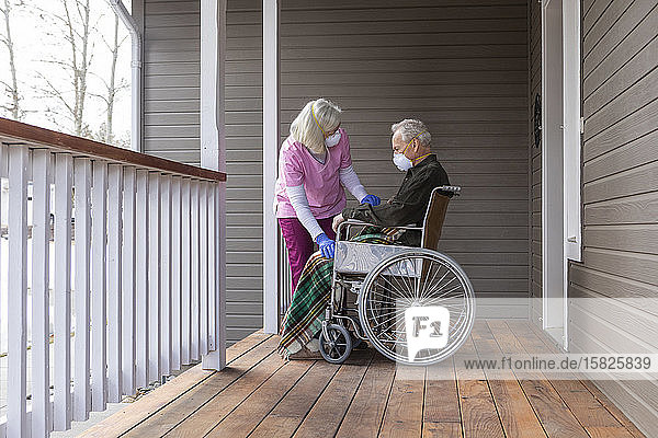 Frau und Mann im Rollstuhl tragen auf der Veranda eine Schutzmaske  um die Übertragung des Coronavirus zu verhindern