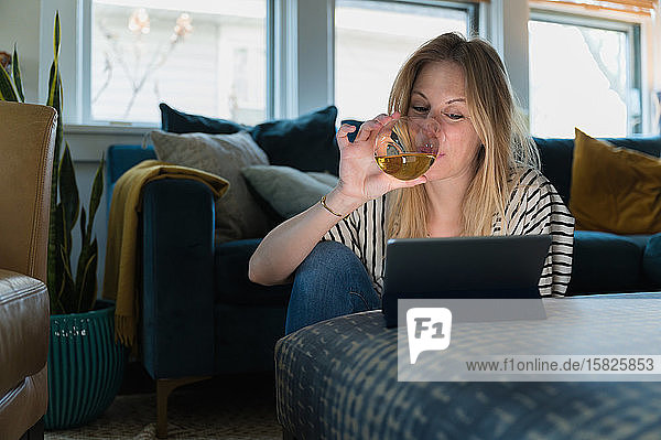 Woman drinking wine and looking at tablet at home