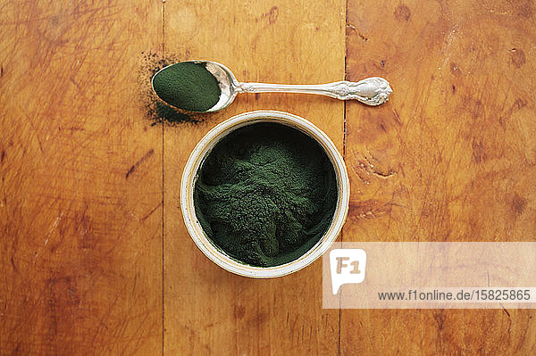 Spirulina in bowl and spoon full against wood