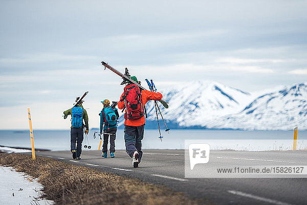 Drei Personen mit Skiern gehen in Island eine Straße entlang