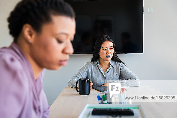 Nachdenkliche Geschäftsfrau benutzt Grafiktablett  während sie mit einem Kollegen im Büro sitzt