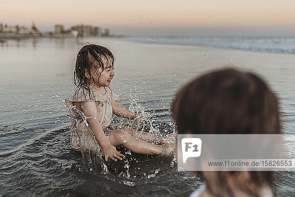 Glückliches 2-jähriges Mädchen planscht am Strand im Wasser