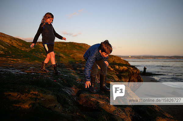 Happy siblings climbing on rocks at sunset near the ocean