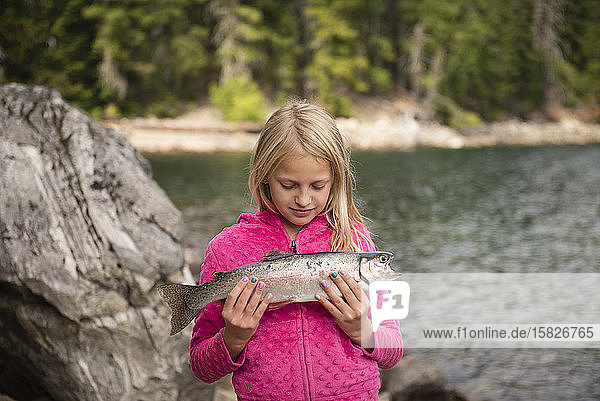 Porträt eines 8-9-jährigen Mädchens  das einen Fisch an einem See hält