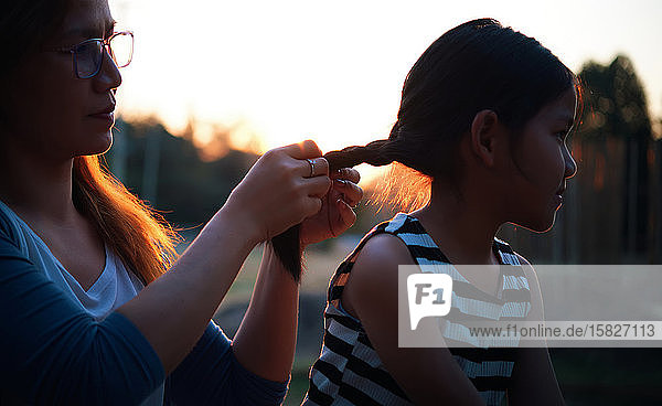 Die Mutter frisiert das Haar ihrer Tochter während des Sonnenuntergangs