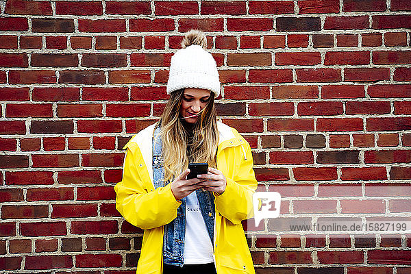 Attraktive blonde Frau mit einem Smartphone an einer Backsteinmauer