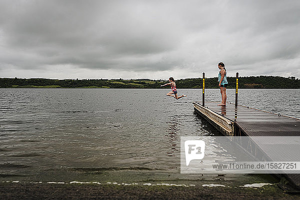 Kleine Mädchen springen an einem bewölkten Sommertag vom Dock in den See