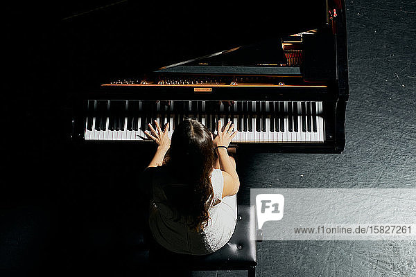 Eine Frau mit braunem Haar in einem weißen Kleid  die auf einem schwarzen Flügel mit erhobenem Deckel spielt. Blick von oben auf den Körper der Pianistin und die Hälfte des Klaviers