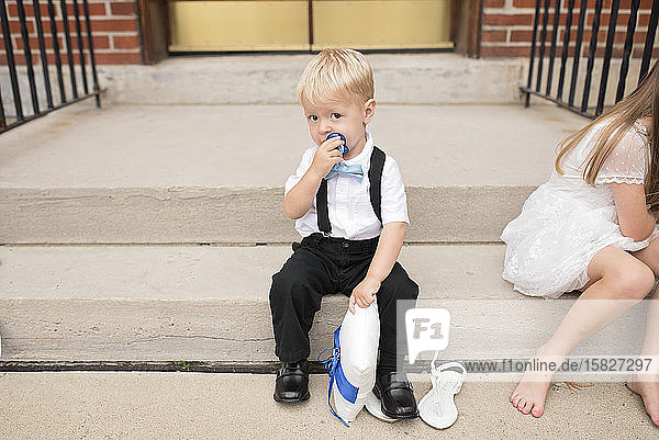 Ring bearer baby sits next to flower girl on steps and looks at camera