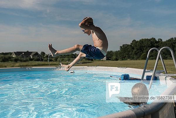 Junge springt an einem sonnigen Sommertag im Garten in den Pool