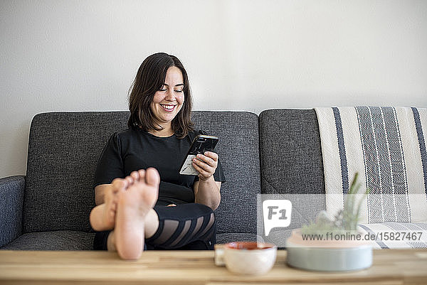 Frau sitzt mit erhobenen Füßen auf der Couch am Telefon