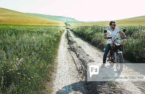 young man parks his motorcycle on the green field road to contemplate