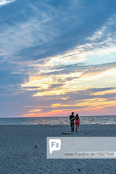Junges Paar auf dem Weg zum Ozean unter wunderschönen Farben des Sonnenuntergangs.
