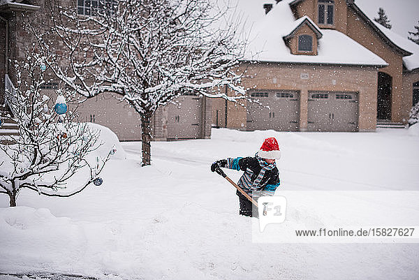 Boy in Santa hat shovelling snow in front yard on a winter day.
