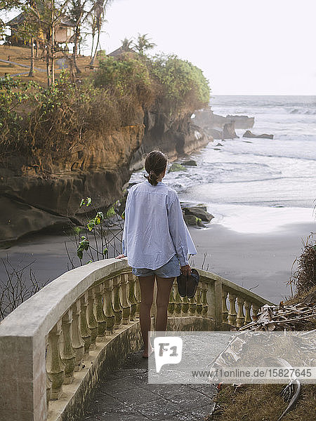 Rückansicht einer Frau  die am Strand eine Treppe hinuntergeht