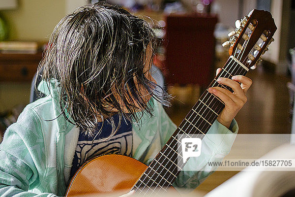 Ein Kind mit Haaren im Gesicht übt klassische Gitarre