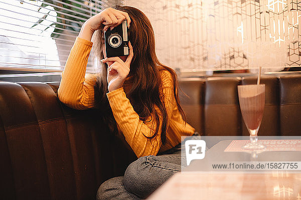 Junge Frau fotografiert mit einer Oldtimer-Kamera  während sie im Café sitzt