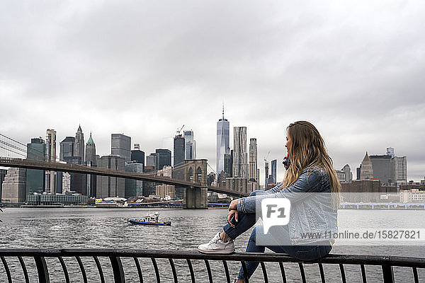Attraktive junge Frau beobachtet die Brooklyn Bridge vom Hudson River in New York City