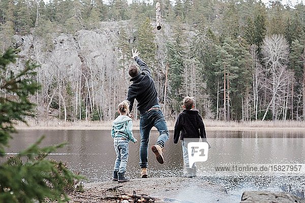 Vater wirft mit seinen Kindern beim Wandern Baumstämme ins Meer