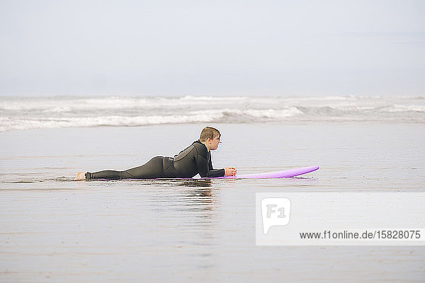 Boy lying on a surfboard on the sand at the beach