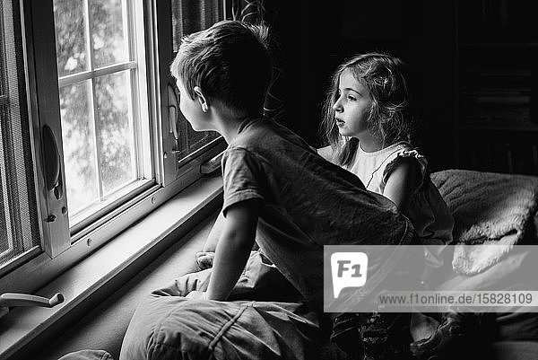 Zwei Kinder sitzen auf einer Couch und schauen aus einem Fenster.