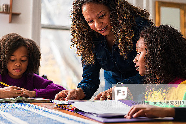 Reife Frau hilft Töchtern beim Lernen am Tisch im Wohnzimmer