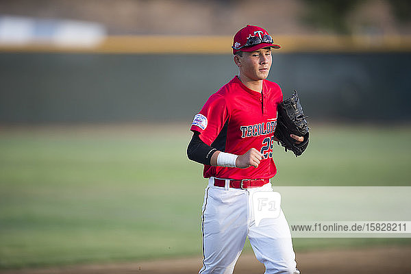 Teen baseball player in red uniform jogging off the field