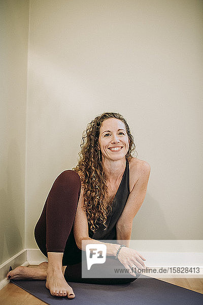 portrait of smiling woman in yoga clothes on mat in a studio