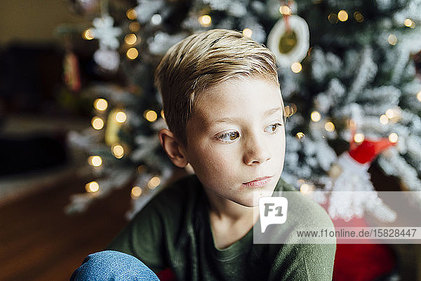 Young boy looking out window next to Christmas tree