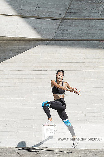 Full body of female athlete in sportswear jumping on concrete