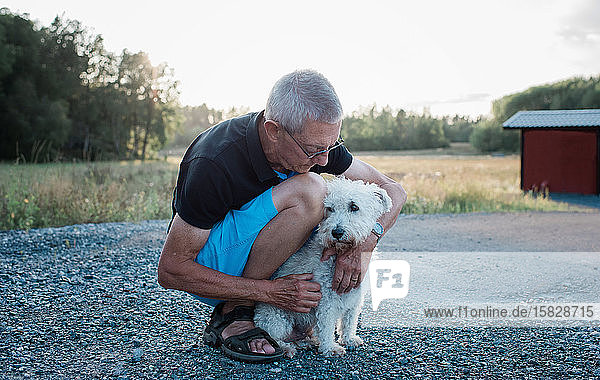 Porträt eines Mannes  der im Sommer beim Spaziergang mit einem Hund kuschelt