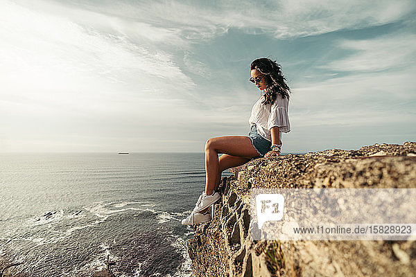 a young woman sitting on the edge of the cliff