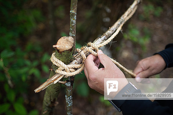 Mann bindet Stöcke mit Schnüren zu einem Baumfort zusammen.