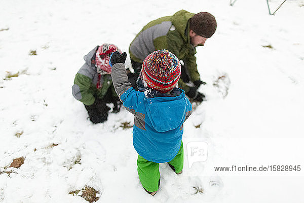 Vater macht im Winter mit zwei Kindern draußen einen Schneeball