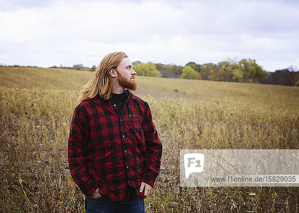 Junger Mann mit langen roten Haaren und Bart draußen auf dem Land
