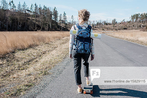 woman carrying a yoga mat in a backpack whilst on a skateboard skating