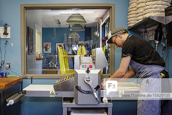 Ein professioneller Bäcker bereitet sich darauf vor  ein Teigblatt durch die Maschine zu ziehen